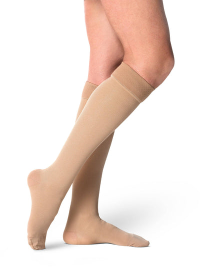 Beige compression stockings being worn on a white background