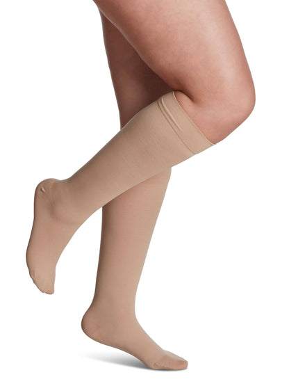 Beige compression stockings being worn on a white background