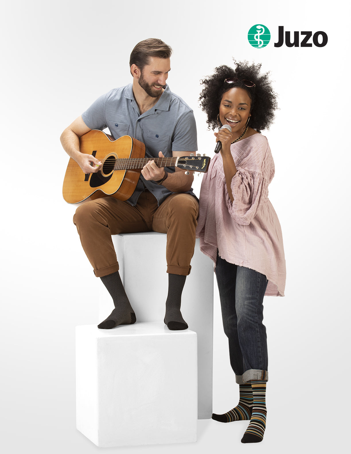 Man playing guitar and woman sitting next to him wearing Juzo compression socks on a white background. Discover the Juzo Compressionsale collection of compression hosiery designed for comfort, support, and everyday wear.