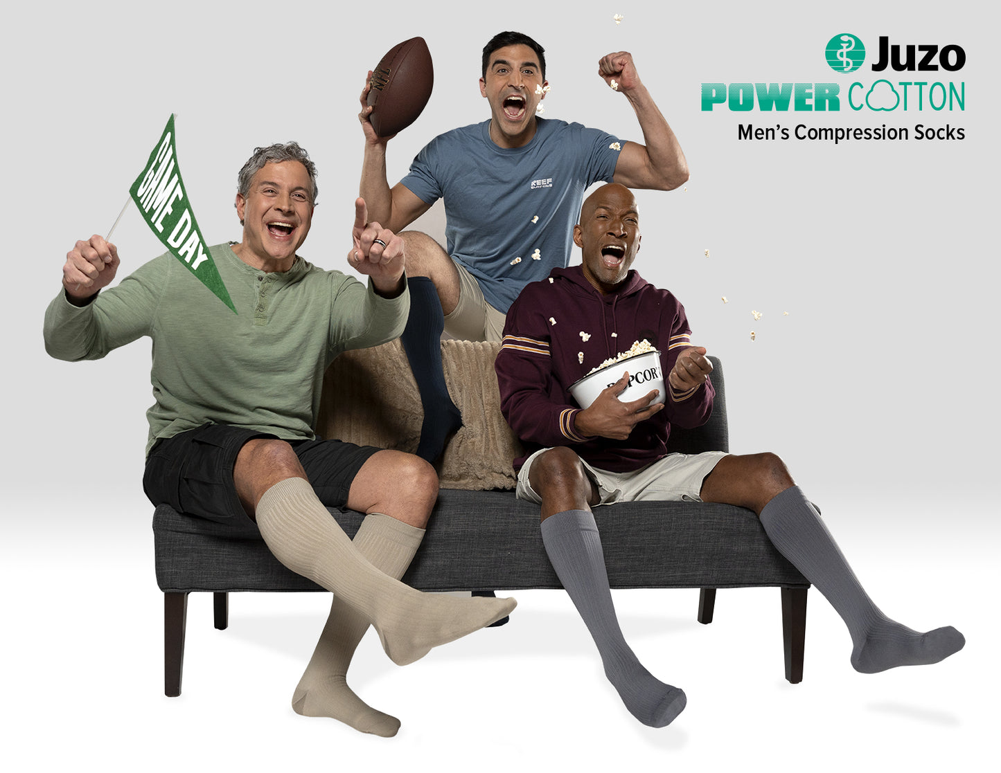 Three men sitting on a couch wearing Juzo compression socks, with sports balls and a flag. Explore the Juzo Compressionsale collection of compression hosiery designed for comfort, support, and active everyday performance.