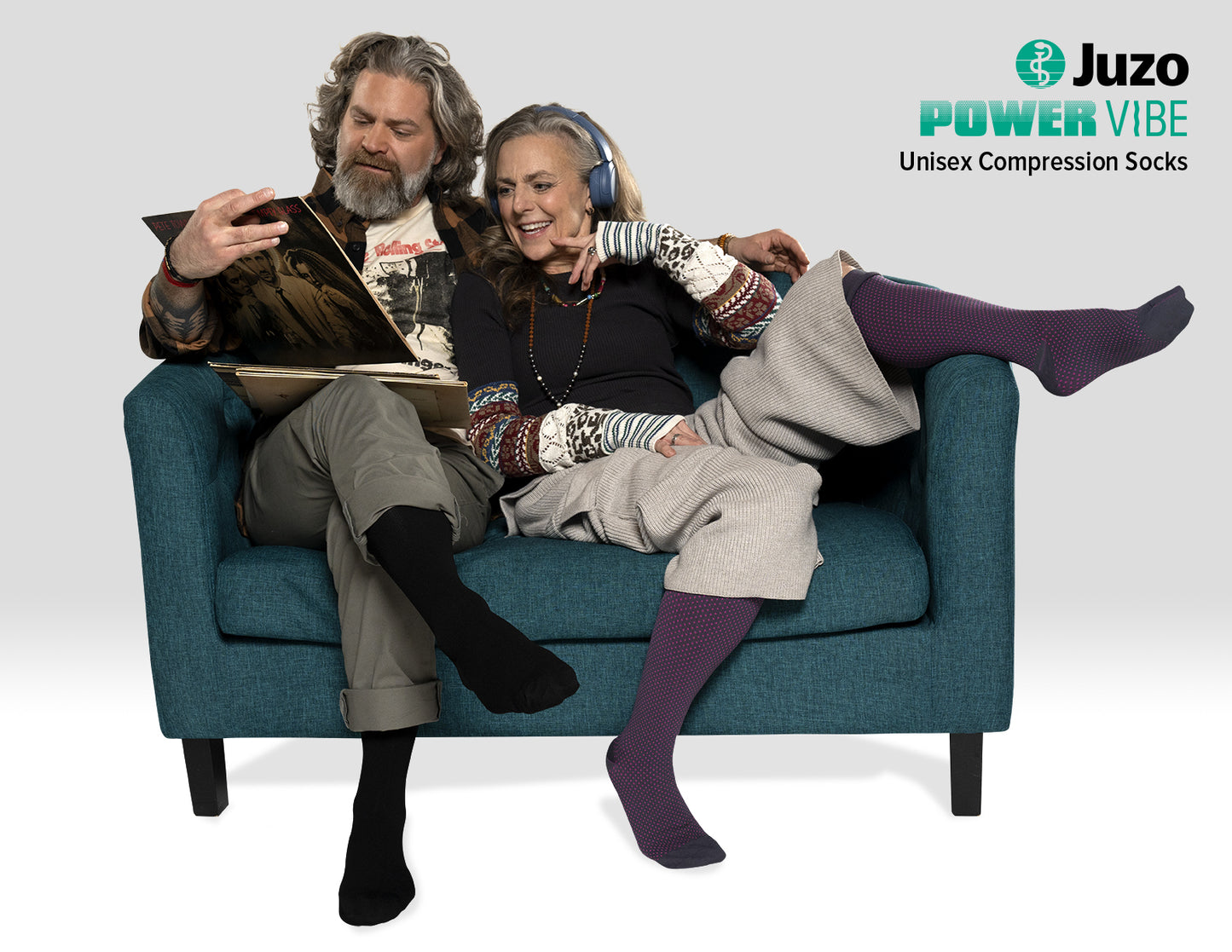 Two people sitting on a couch wearing Juzo Power Vibe compression socks, with the brand logo visible – Compressionsale compression wear for everyday comfort and leg support.