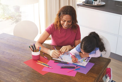 Woman and child sitting at a table with art supplies, smiling and engaged in an activity.