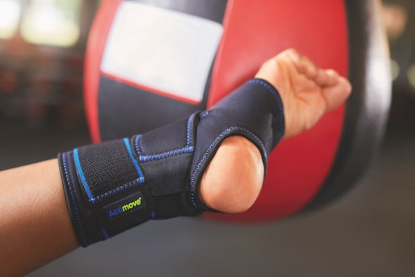 Hand wearing a black wrist support brace from Compressionsale with a blurred red and white background