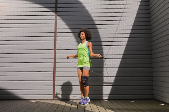 Woman exercising with a jump rope against a gray wall
