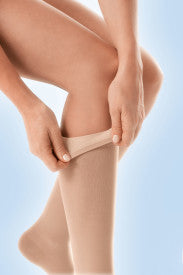 Person wearing beige compression stockings against a light blue background