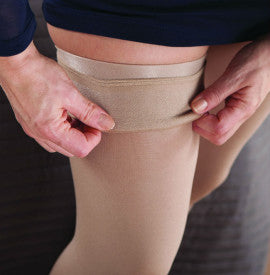 Person adjusting a beige compression garment on their leg.