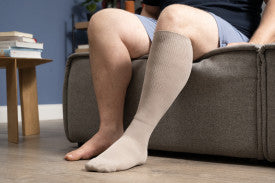 Person sitting on a couch wearing beige knee-high socks.