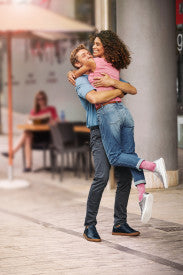 Woman holding a child on a city street with people sitting at tables in the background from Compressionsale."